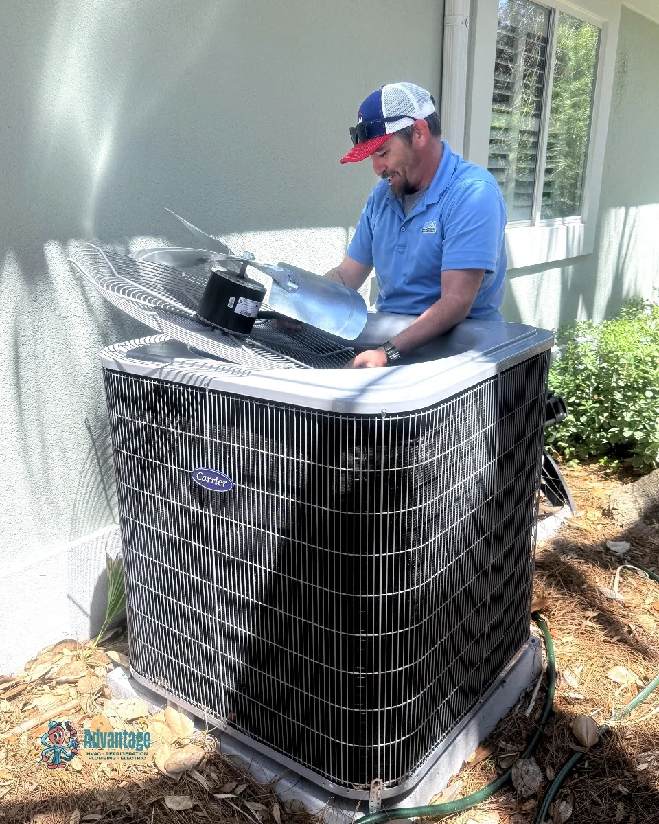 Advantage technician cleaning and inspecting a Carrier outdoor AC unit with the fan top lifted during a seasonal AC tune-up on the Emerald Coast