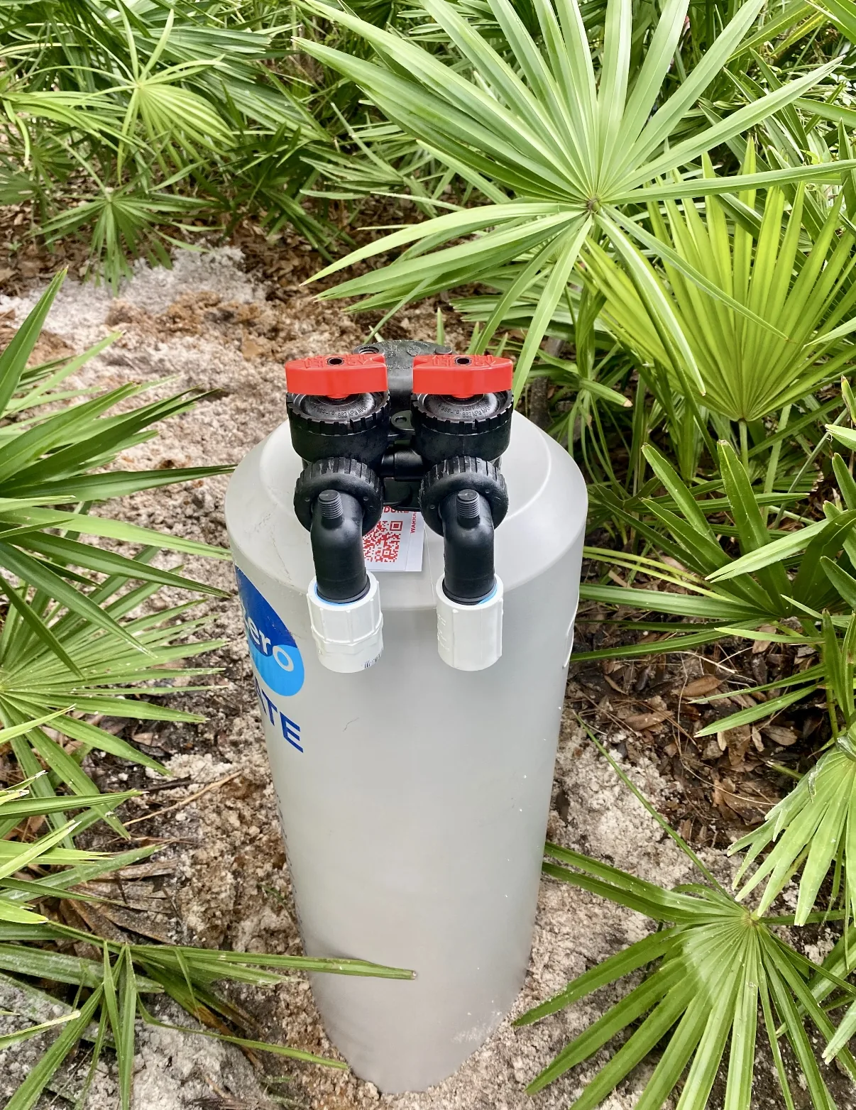 Whole-home water softener and filtration system installed outside a Fort Walton Beach home among native saw palmettos